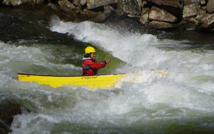 A person wearing safety gear paddles a yellow canoe through rapids. 